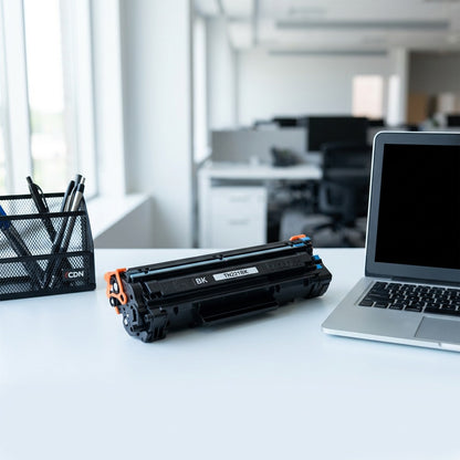 Black TN221BK toner cartridge shown for scale next to a laptop and desk organizer in an office.