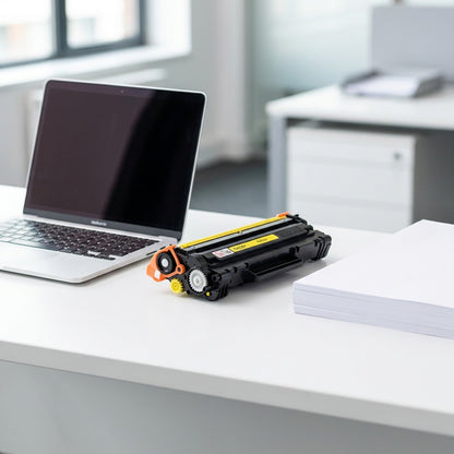 Brother TN225Y Yellow Toner Cartridge on an office desk next to a laptop for scale.