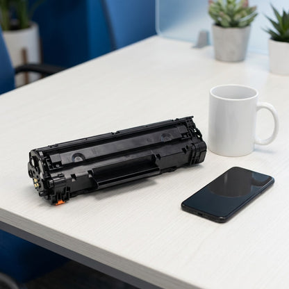 HP 206A Black Remanufactured Toner Cartridge shown on a desk beside a coffee mug and a smartphone.