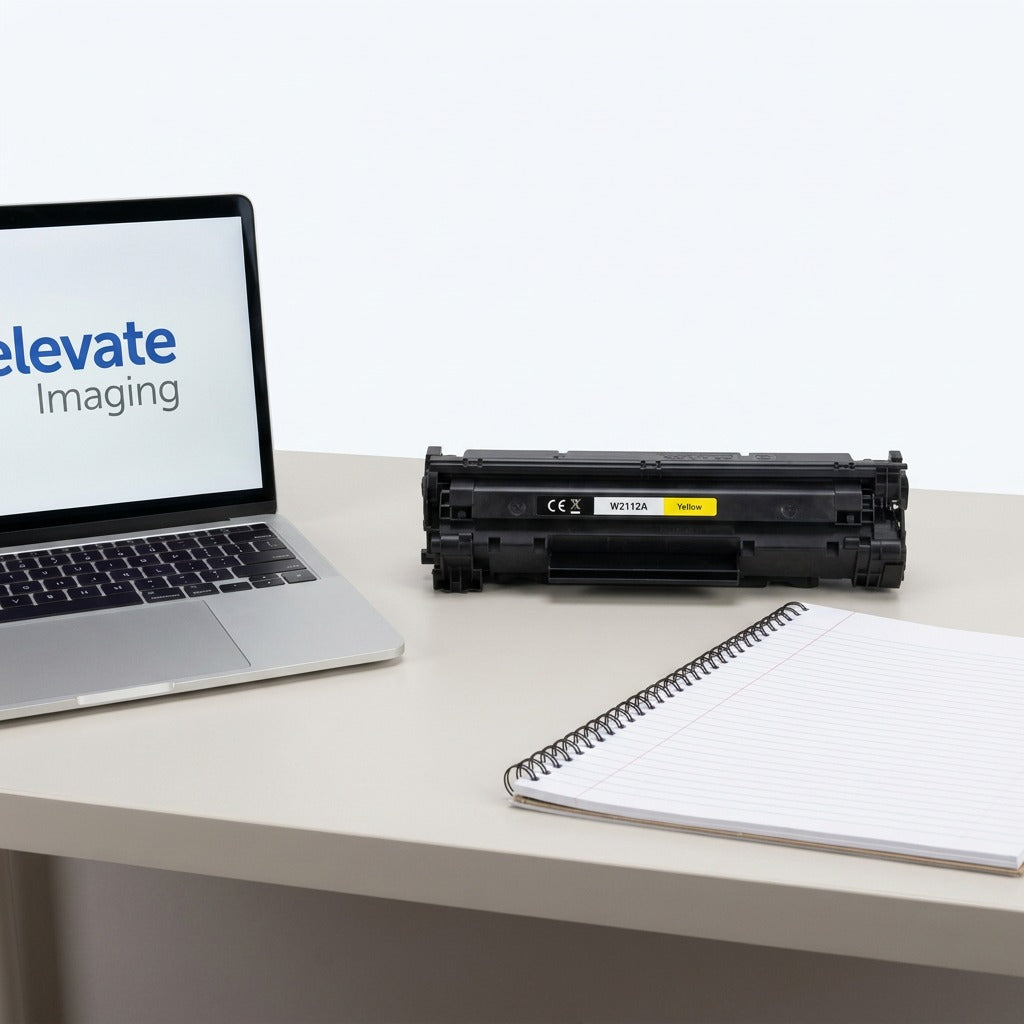 Yellow HP 206A (W2112A) remanufactured toner cartridge on a desk next to a laptop for scale.