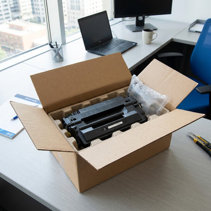 A compatible HP 55X CE255X black toner cartridge securely packaged in a shipping box on an office desk.
