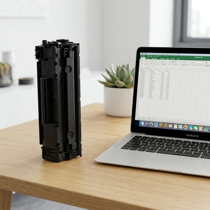 An HP 649X (CE260X) black toner cartridge standing vertically on a desk next to a laptop for scale.