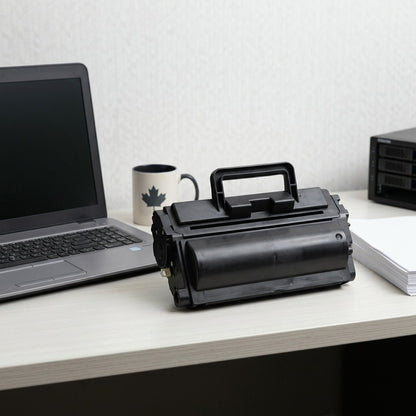 Compatible HP 90A (CE390A) black laser toner cartridge on a desk next to a laptop for scale.