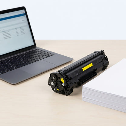 HP 507A CE402A yellow toner cartridge on a desk next to a laptop and paper stack for scale.