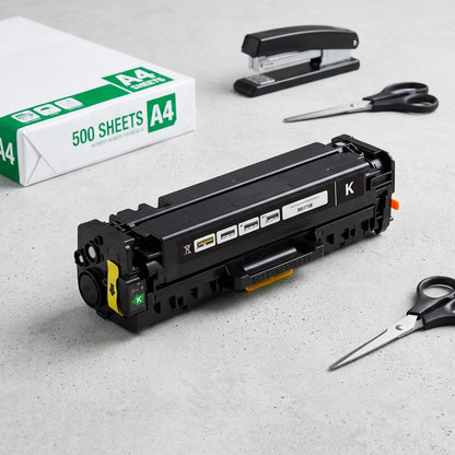 Black HP 305A (CE410A) toner cartridge on a desk with A4 paper and office supplies for scale.
