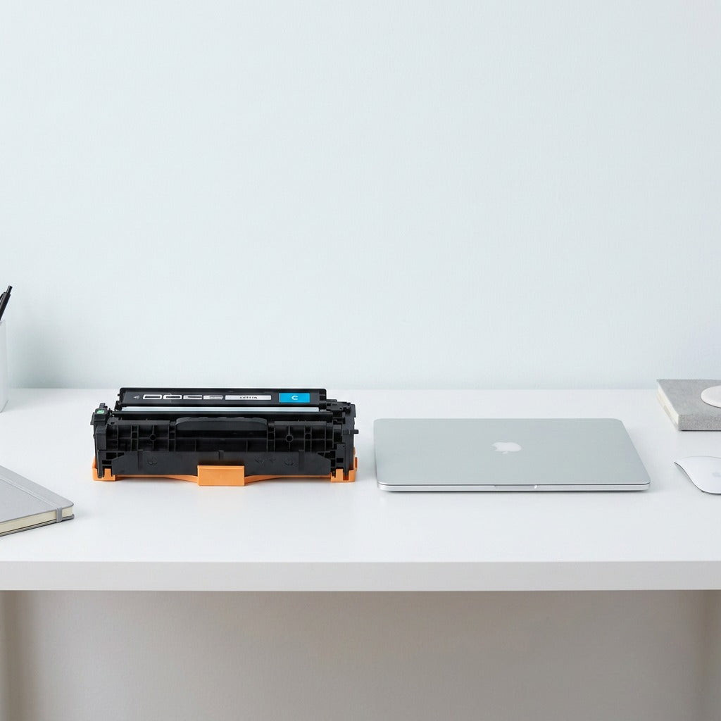 Scale reference of Elevate HP 305A (CE411A) Cyan Toner Cartridge beside a laptop on a white desk.