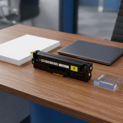 Yellow HP 305A (CE412A) toner cartridge on a desk next to a laptop and paper for scale reference.