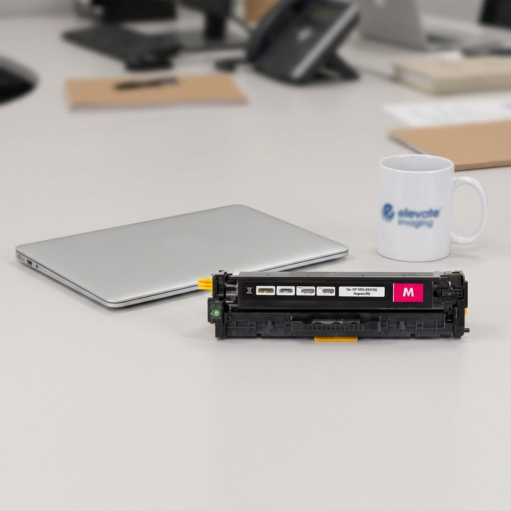 HP 305A Magenta Toner Cartridge on a desk next to a laptop and coffee mug for scale reference.