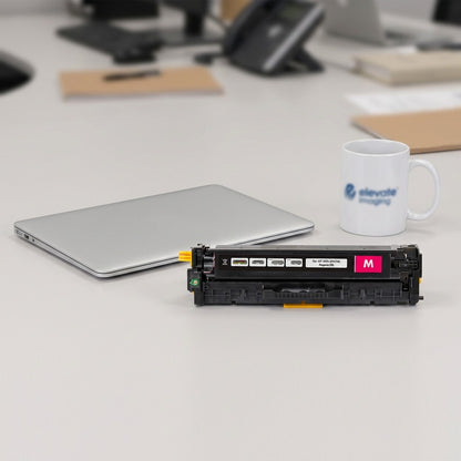 HP 305A Magenta Toner Cartridge on a desk next to a laptop and coffee mug for scale reference.