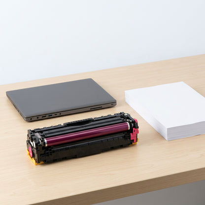 Magenta HP 131A (CF213A) toner cartridge on a desk beside a laptop and a stack of A4 paper for scale.