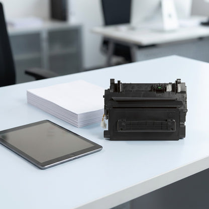 Scale reference for HP CF281A toner cartridge beside a tablet and paper on a desk.