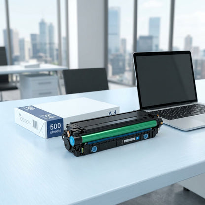 HP 508A (CF361A) cyan toner cartridge next to a silver laptop and A4 paper for scale on a desk.