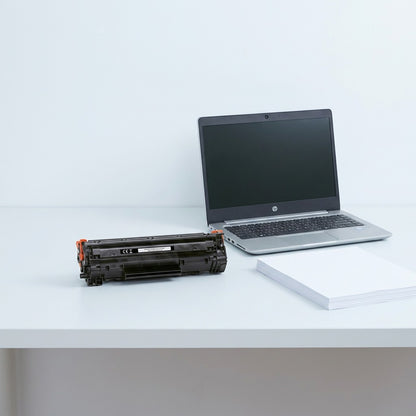 HP 201X CF400X black toner cartridge on a desk next to 14-inch laptop and A4 paper for scale.