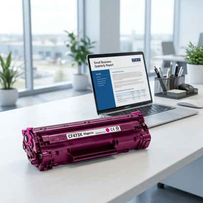 HP 73X CF473X Magenta Toner Cartridge on an office desk next to a laptop for scale reference.